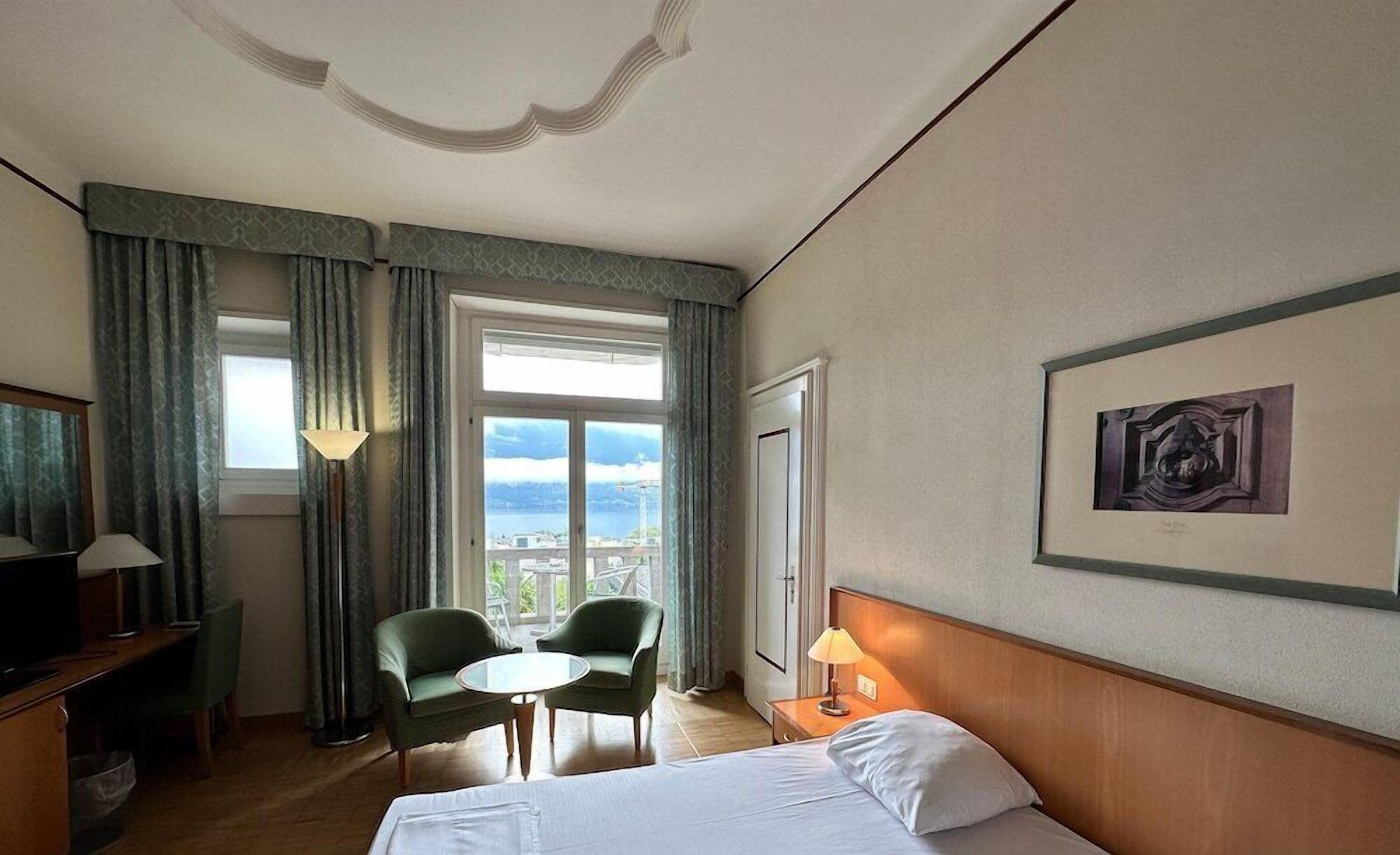 A hotel room with a bed, two chairs, a small table, a lamp, a TV, and a window with a view.