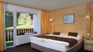A bedroom with a large bed, wooden walls, a painting, and a view of a garden through a sliding door.