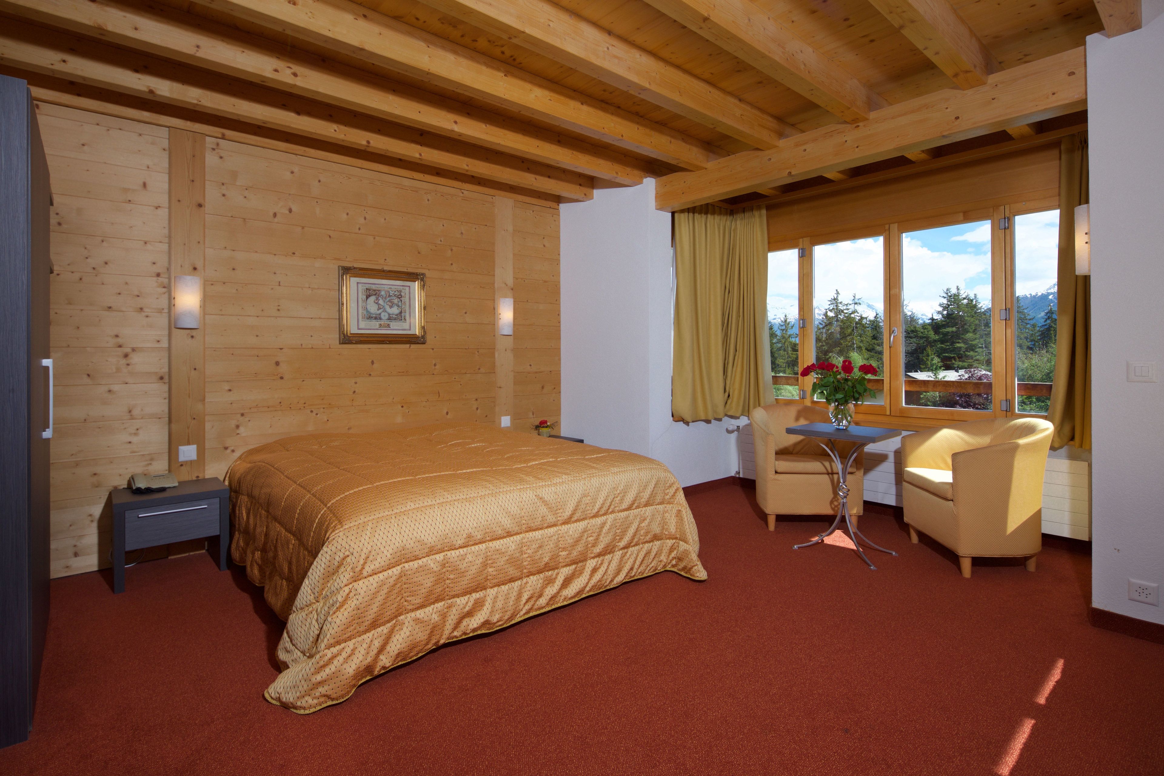 Une chambre avec un plafond en bois, un lit, un bureau, une chaise et une fenêtre avec des rideaux.
