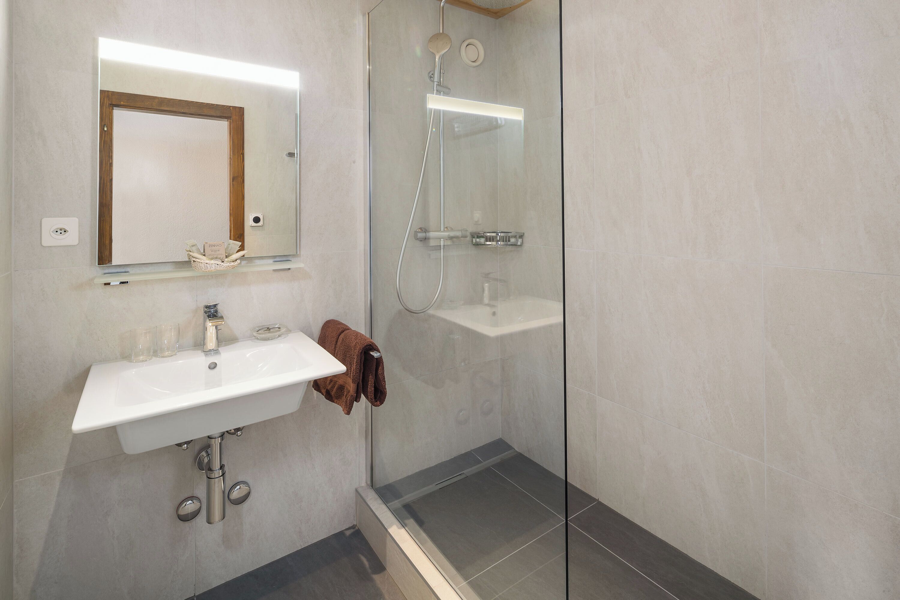 A bathroom with a white sink, a mirror, a glass shower enclosure, and a towel hanging on the wall.
