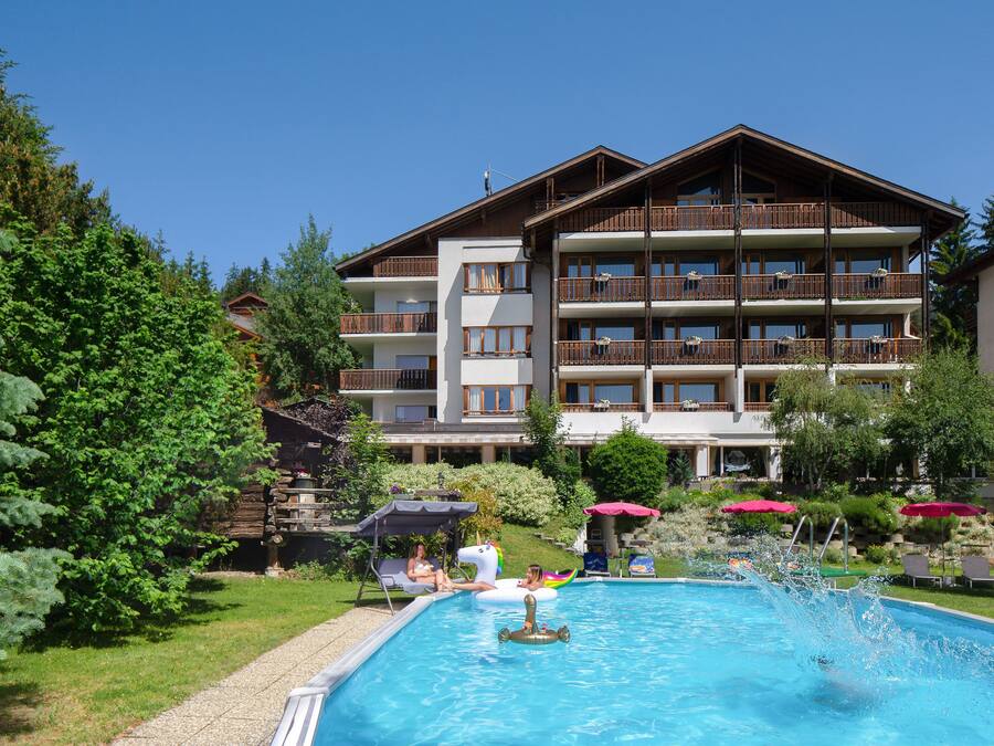 A hotel with a swimming pool, surrounded by greenery and a multi-story building with balconies.