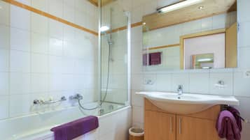 Un baño moderno con ducha envuelta en vidrio, una bañera, un mueble de tocador de madera con lavabo y un espejo sobre el lavabo.