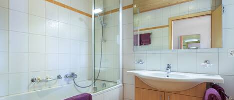 A modern bathroom with a glass-enclosed shower, a bathtub, a wooden vanity with a sink, and a mirror above the sink.
