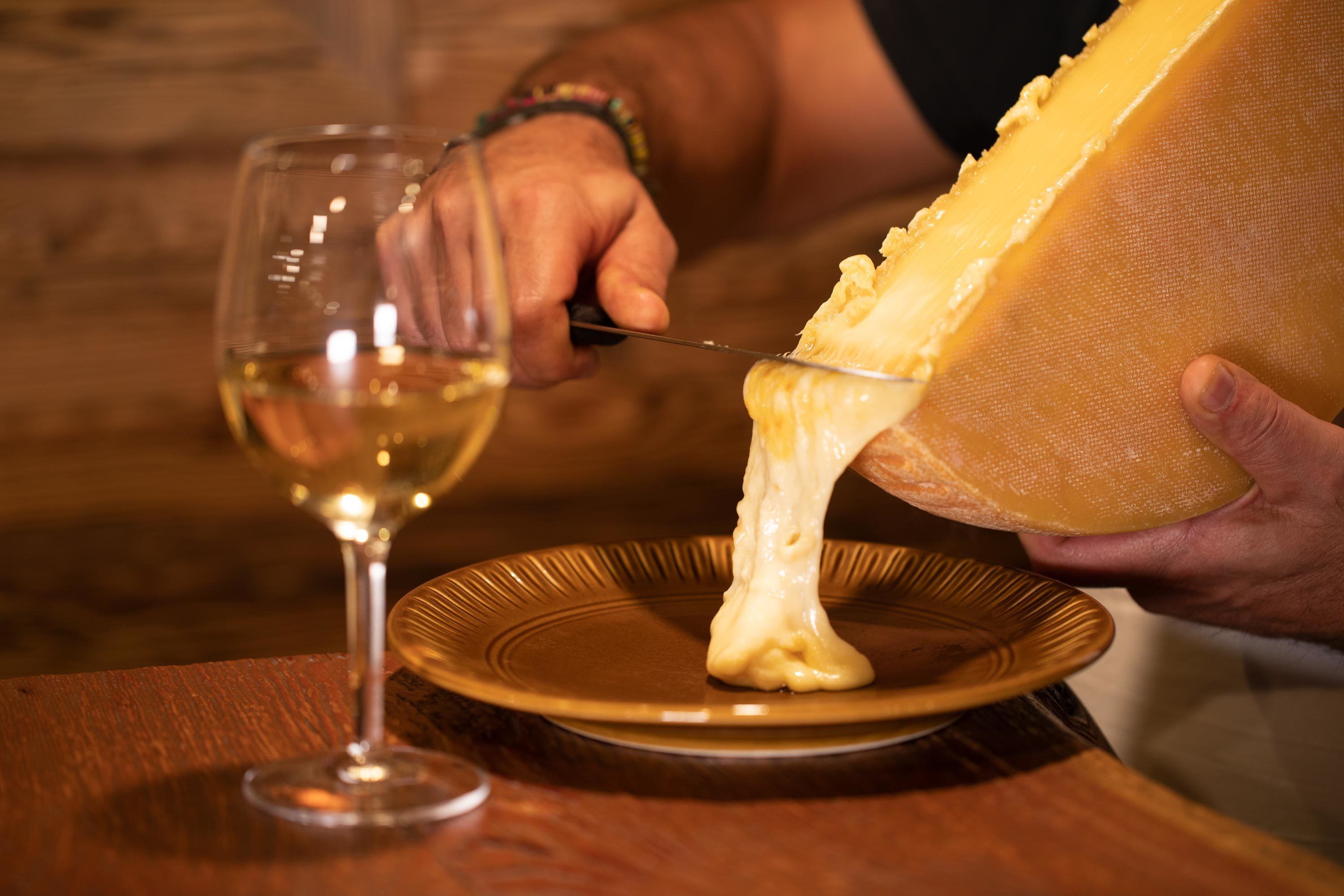 A person cutting a large wheel of cheese on a plate.