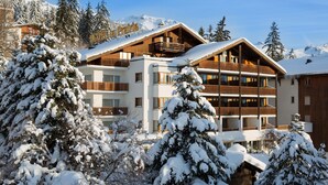 A hotel with multiple balconies and a snowy mountain backdrop. - La Prairie (Crans-Montana)