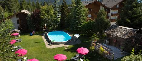 A pool area with lounge chairs and umbrellas, surrounded by greenery and mountain views.