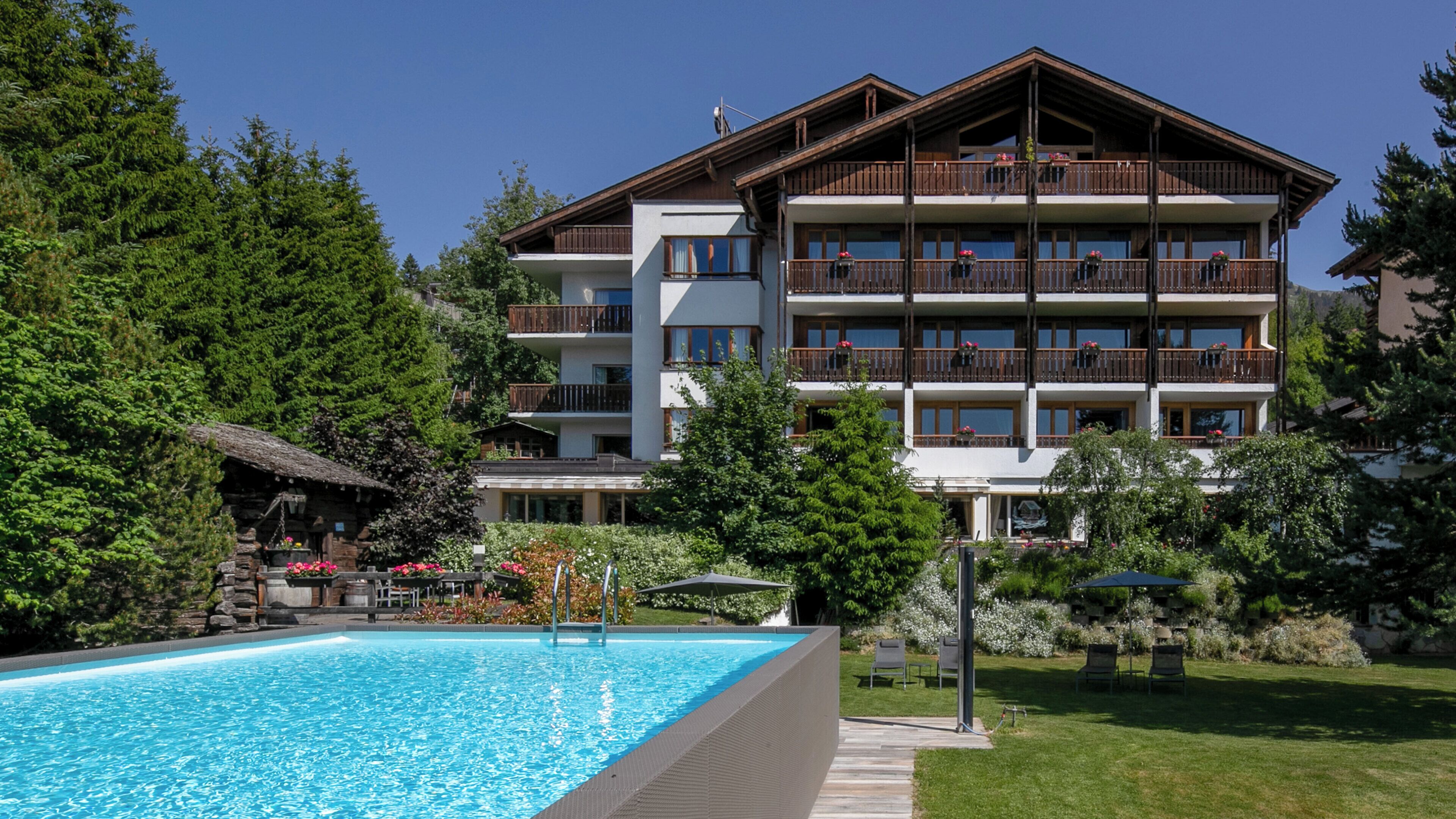 A multi-story hotel with a pool, surrounded by lush greenery and trees.