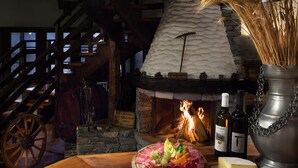A rustic interior with a stone fireplace, wooden furniture, and a variety of food items including cheese, grapes, and meats. - La Prairie (Crans-Montana)