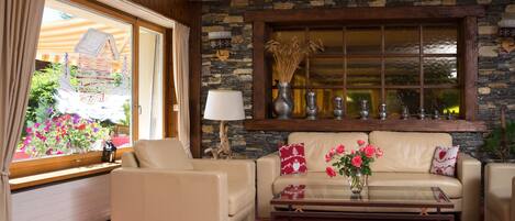 A cozy living room with a stone wall, a sofa, a coffee table, and a window with a view of flowers.