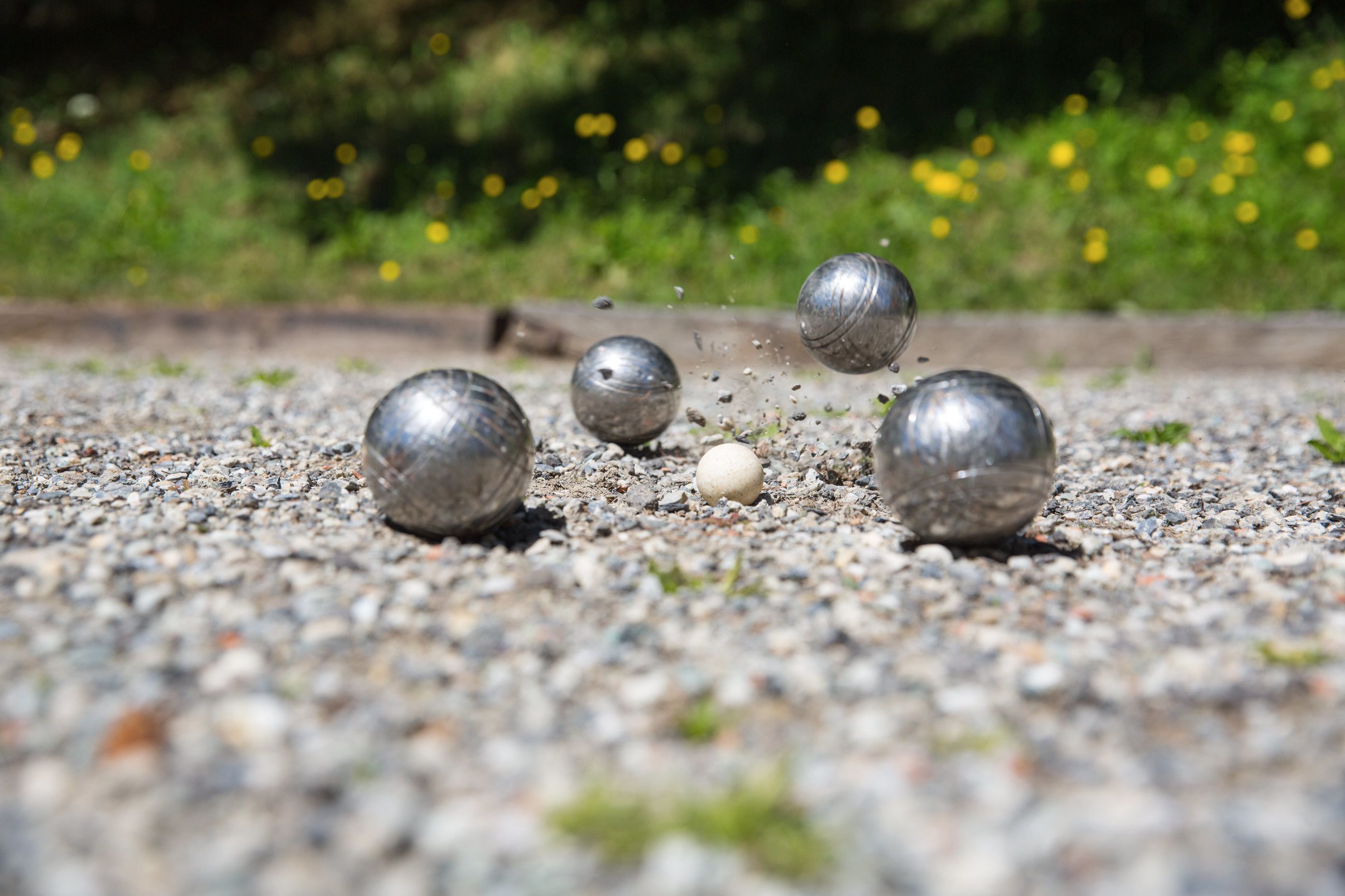 Primi piani di sfere metalliche su un letto di ghiaia, con uno sfondo naturale sfocato.