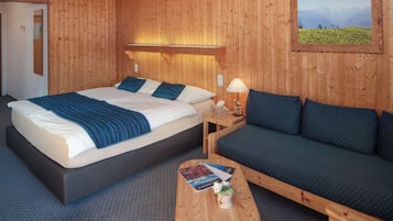 Una habitación con paneles de madera, una cama, un sofá y una pequeña mesa con una lámpara y libros.