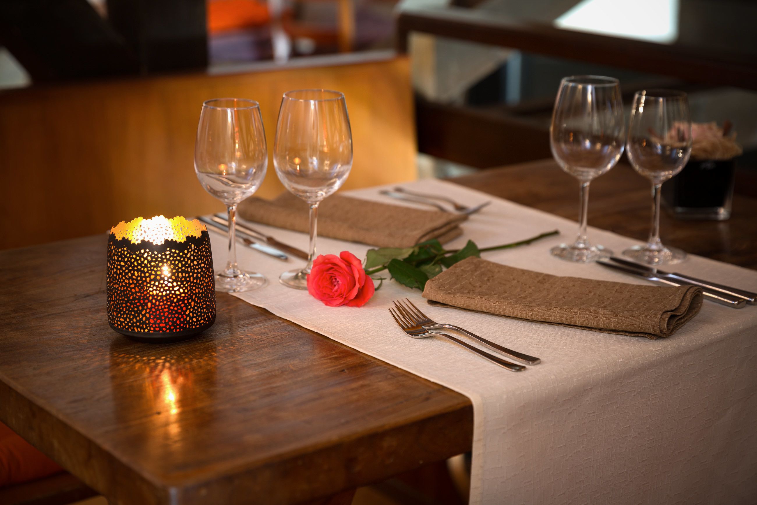 Une table à manger dressée avec deux verres à vin, une bougie et une rose.