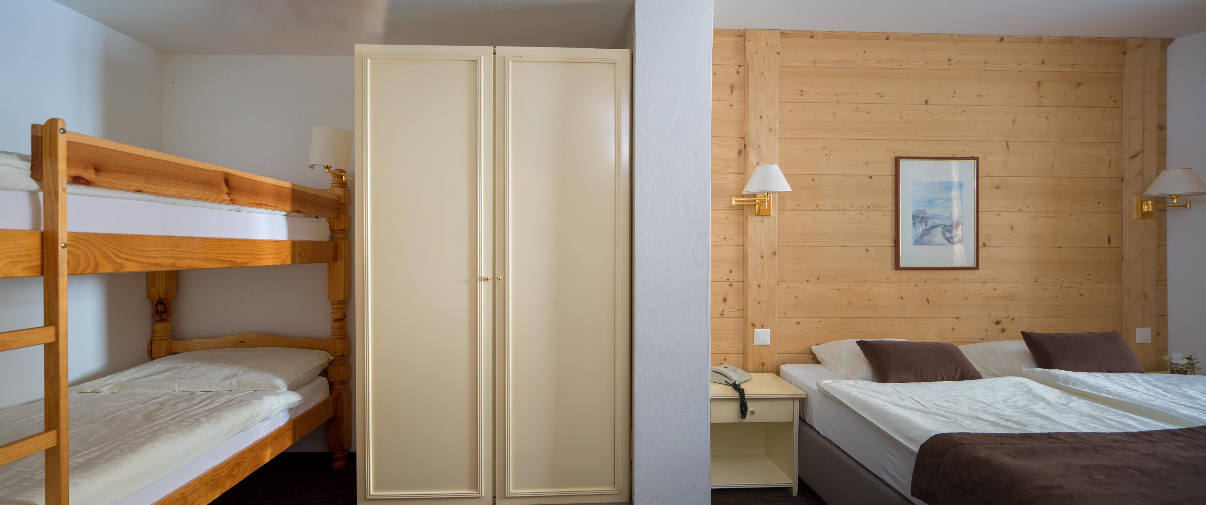 Et værelse med køjeseng, garderobeskab, skrivebord med lampe og en seng med puder.