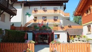 A hotel with a white facade, wooden balconies with flower boxes, and a red entrance.