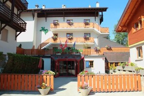 Un hotel con fachada blanca, balcones de madera con jardineras de flores y una entrada roja.
