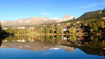 Une ville au bord d’un lac, avec des bâtiments dont les façades se reflètent dans l’eau, le tout entouré de montagnes.