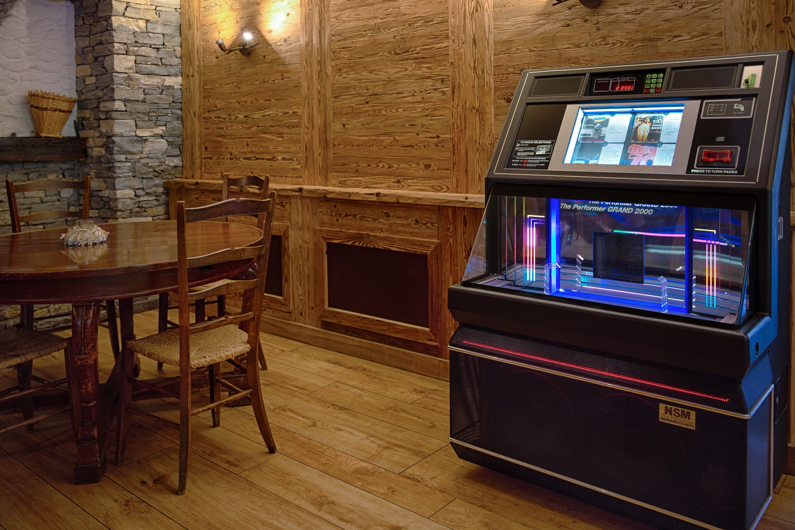 A wooden interior with a table and chairs, a fireplace, and a jukebox.