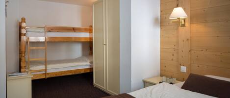 Une chambre avec un lit superposé, une armoire, une table de chevet avec une lampe et un téléphone.