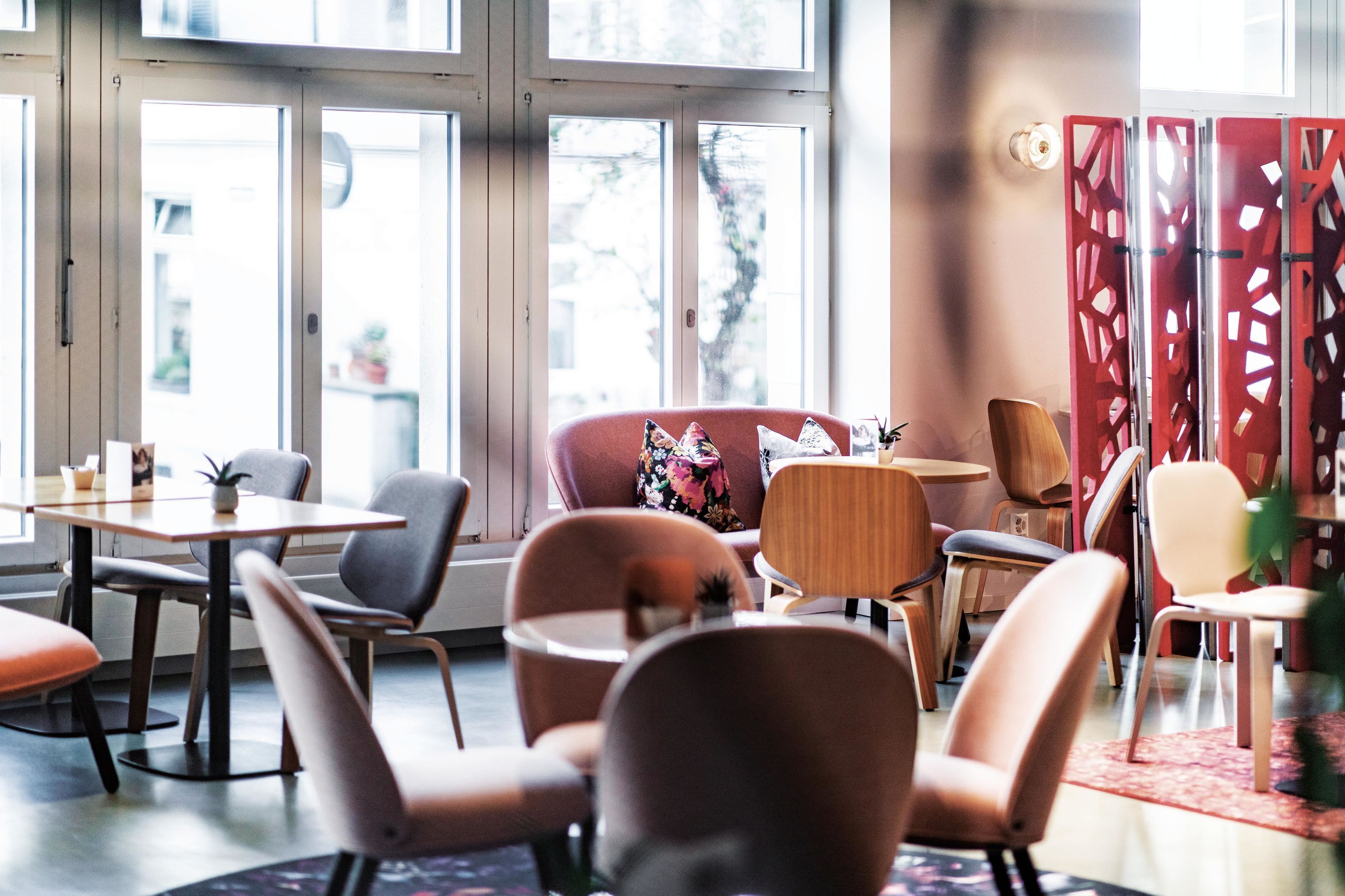 A modern interior with a mix of seating options including chairs and a sofa, large windows, and a decorative partition.