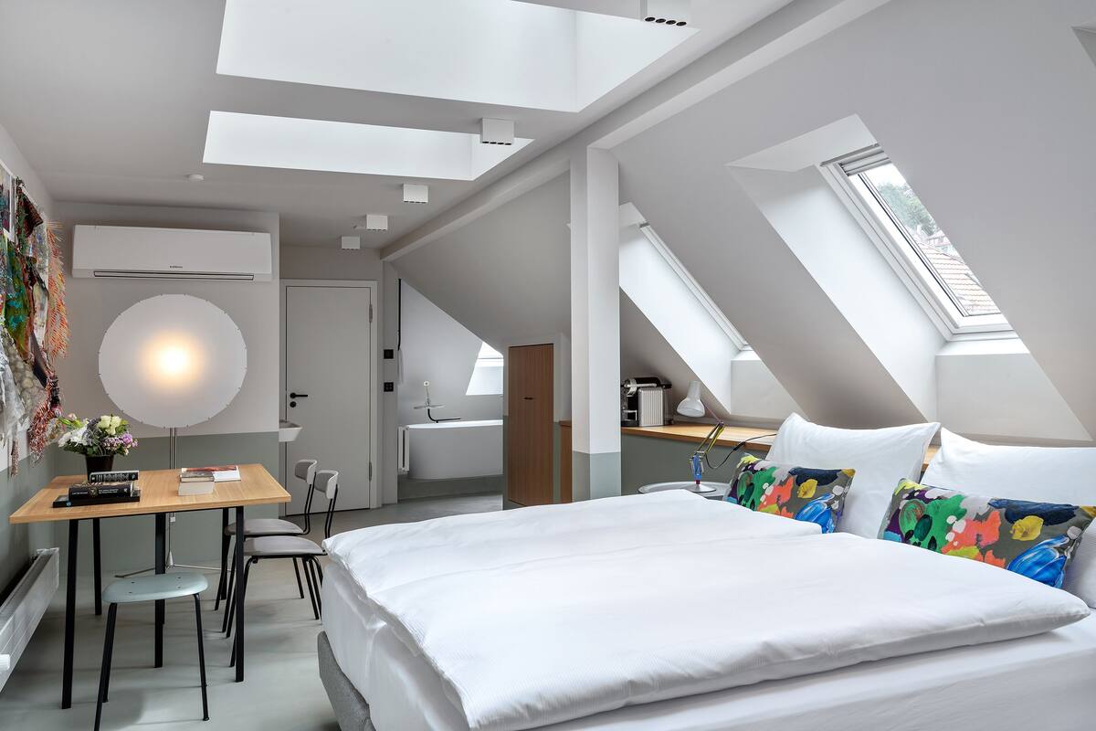 A modern bedroom with a skylight, a desk with a chair, and a bed with colorful pillows.