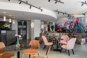 Un interior moderno con una mesa redonda, sillas, un jarrón con flores, un sofá y un mural colorido en la pared.