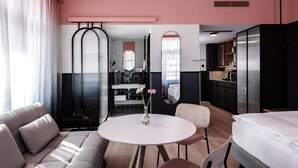 A modern hotel room with a sofa, a round table with a vase, a bed, and a kitchenette. -  Sorell Boutique-Hotel City Weissenstein St. Gallen (St. Gallen)