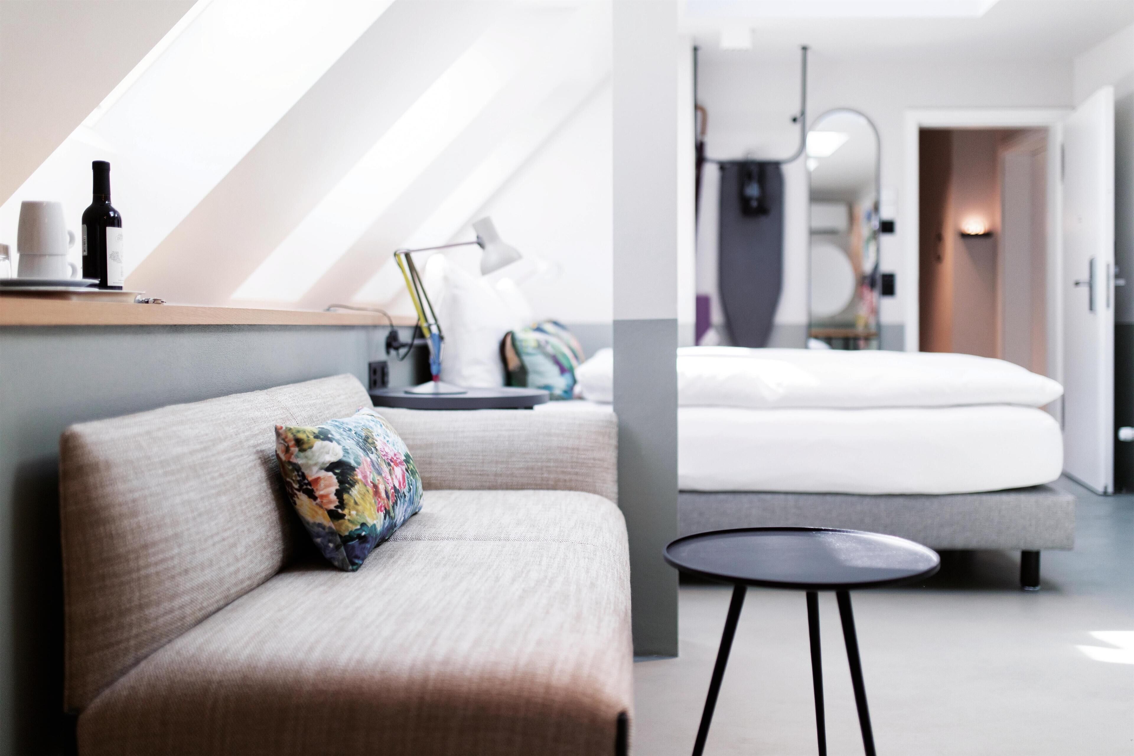 Une chambre d’hôtel moderne avec un canapé, une petite table ronde, un lit et une table de chevet avec une lampe.