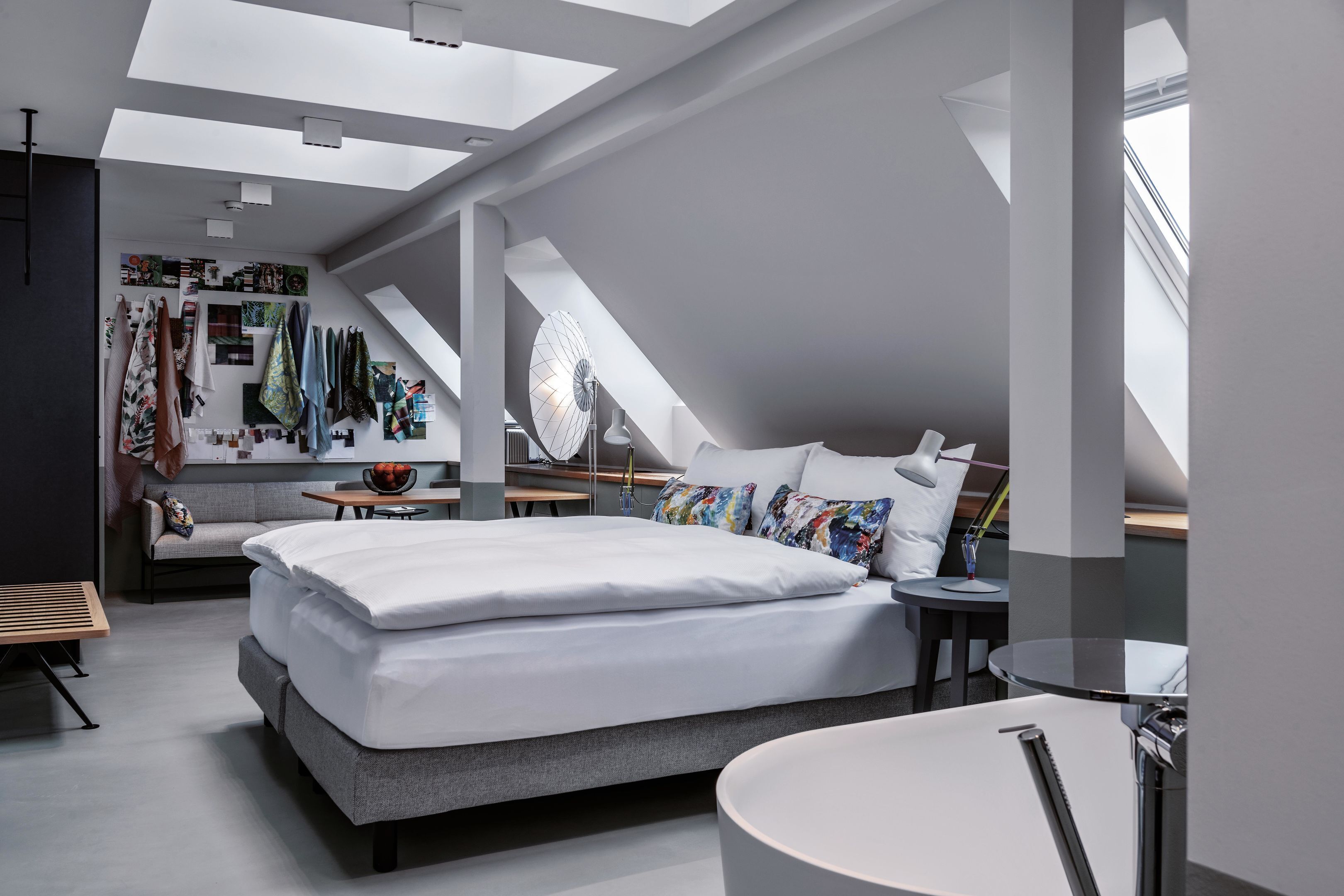 A modern bedroom with a large bed, a desk, a round table, and a skylight.