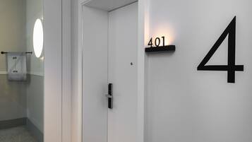 Een modern interieur met een witte deur, het getal '401' verlicht op de muur, en een handdoek aan een haak.