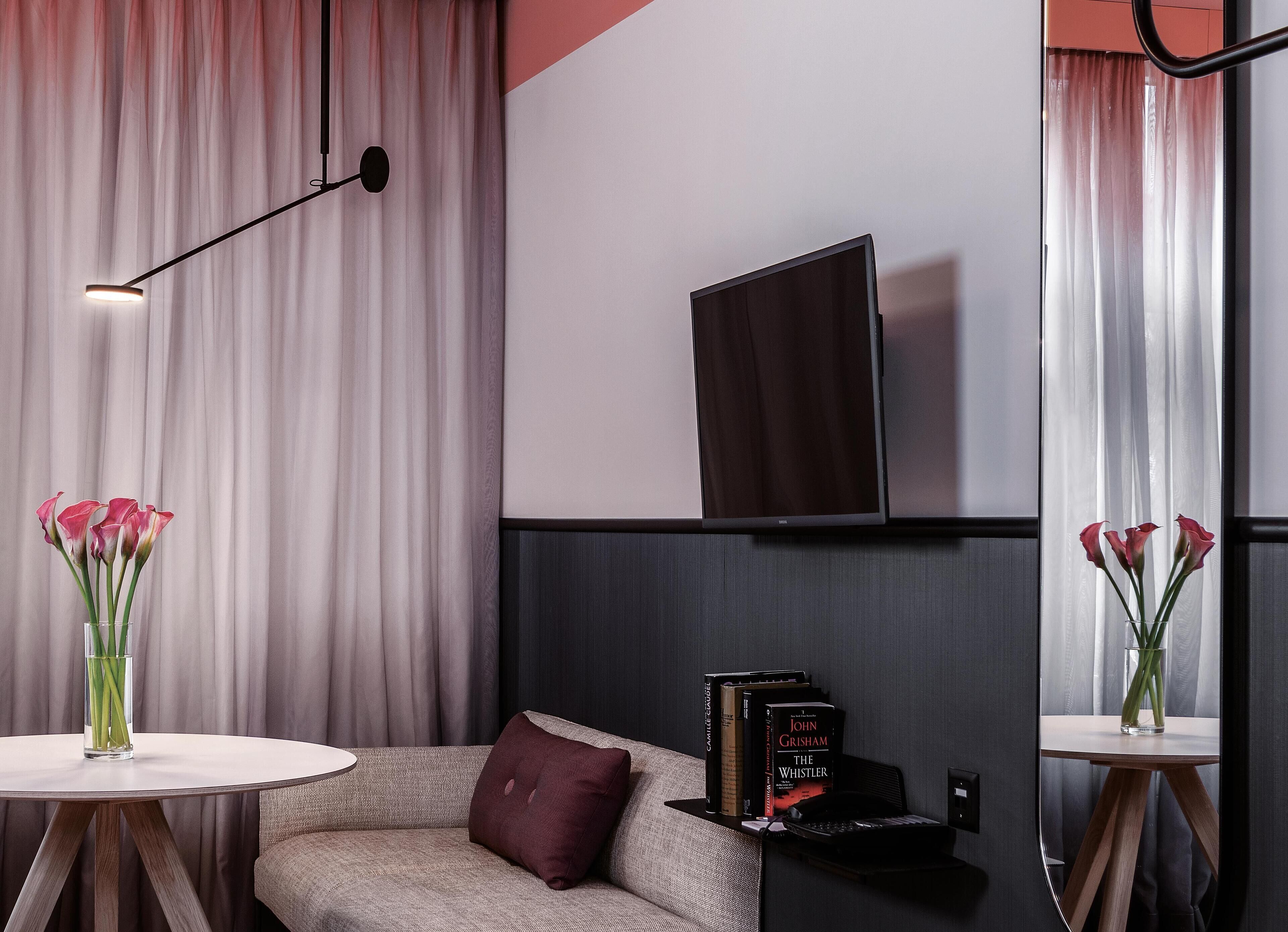 Ein modernes Wohnzimmer mit einer Couch, einem Couchtisch, einem flachbildfernseher an der Wand und zwei Vasen mit Blumen.