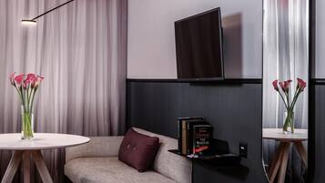 Ein modernes Wohnzimmer mit einer Couch, einem Couchtisch, einem flachbildfernseher an der Wand und zwei Vasen mit Blumen.