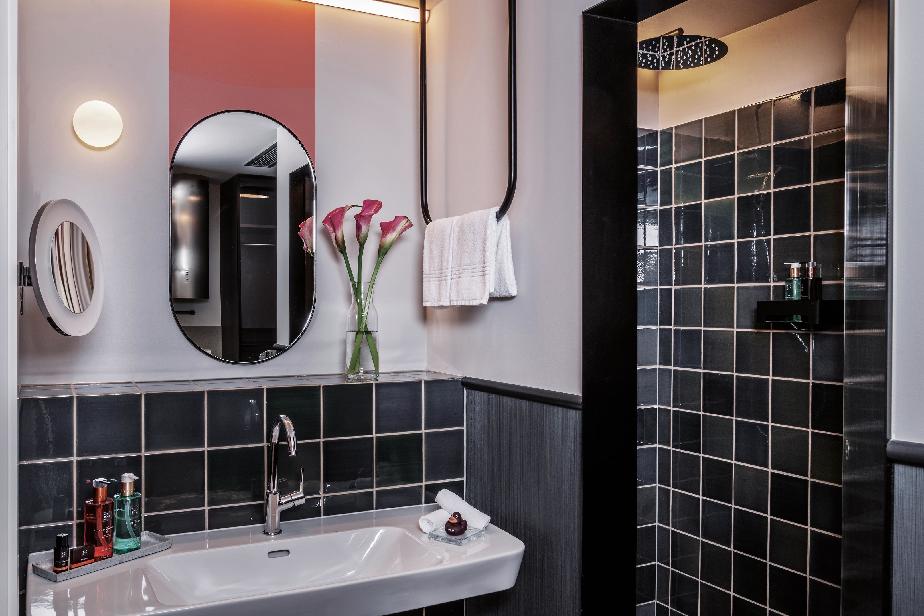 Ein modernes Badezimmer mit einem weißen Waschbecken, einem Spiegel, einem Handtuchhalter und einer Duschkabine.
