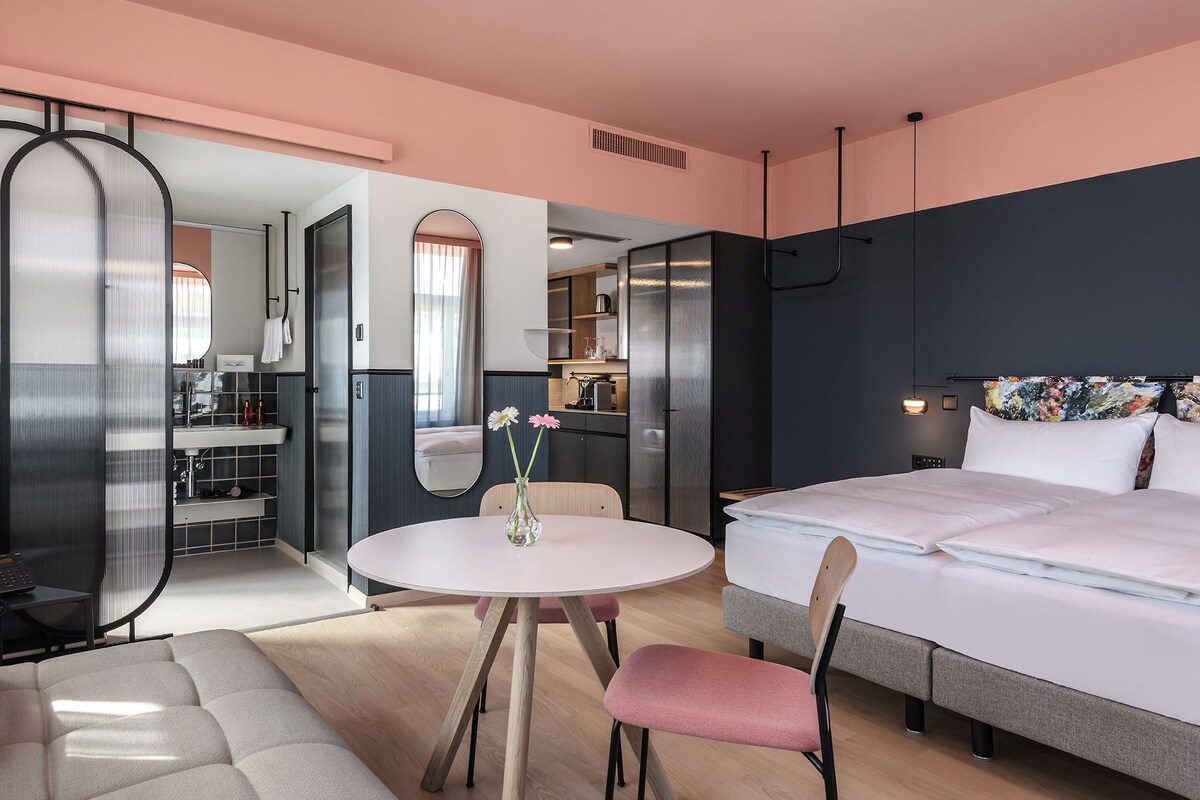Een moderne hotelkamer met een bed, een ronde eettafel met stoelen, een bank en een spiegel.