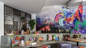 A modern living room with a large abstract painting, a bookshelf, and colorful cushions. -  Sorell Boutique-Hotel City Weissenstein St. Gallen (St. Gallen)