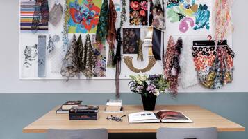 A room with a wooden table, two chairs, a vase with flowers, and a wall decorated with various fabric pieces and artwork.