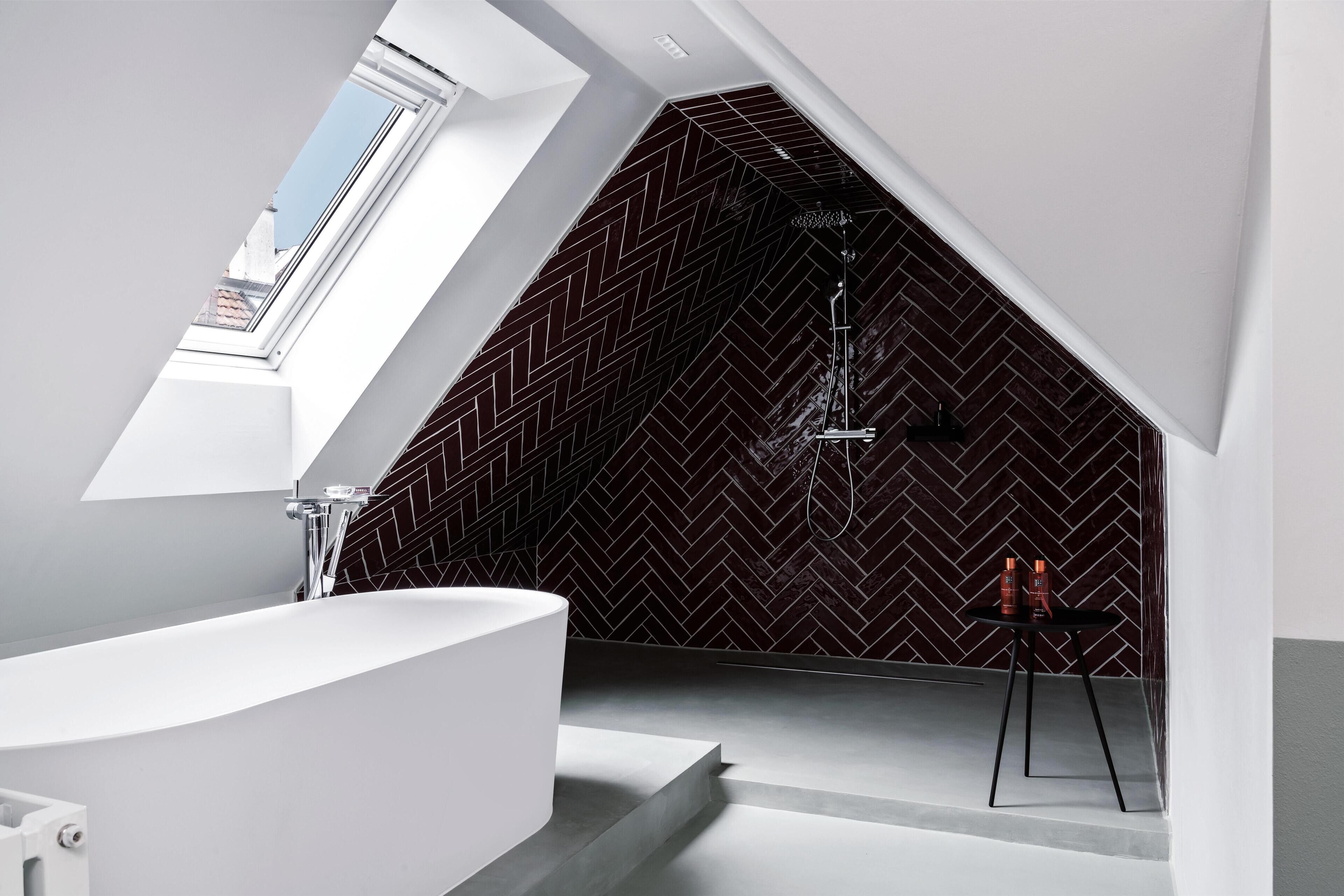 Un bagno moderno con una parete a motivi a spina di pesce, una vasca freestanding e un piccolo tavolo con articoli da toilette.