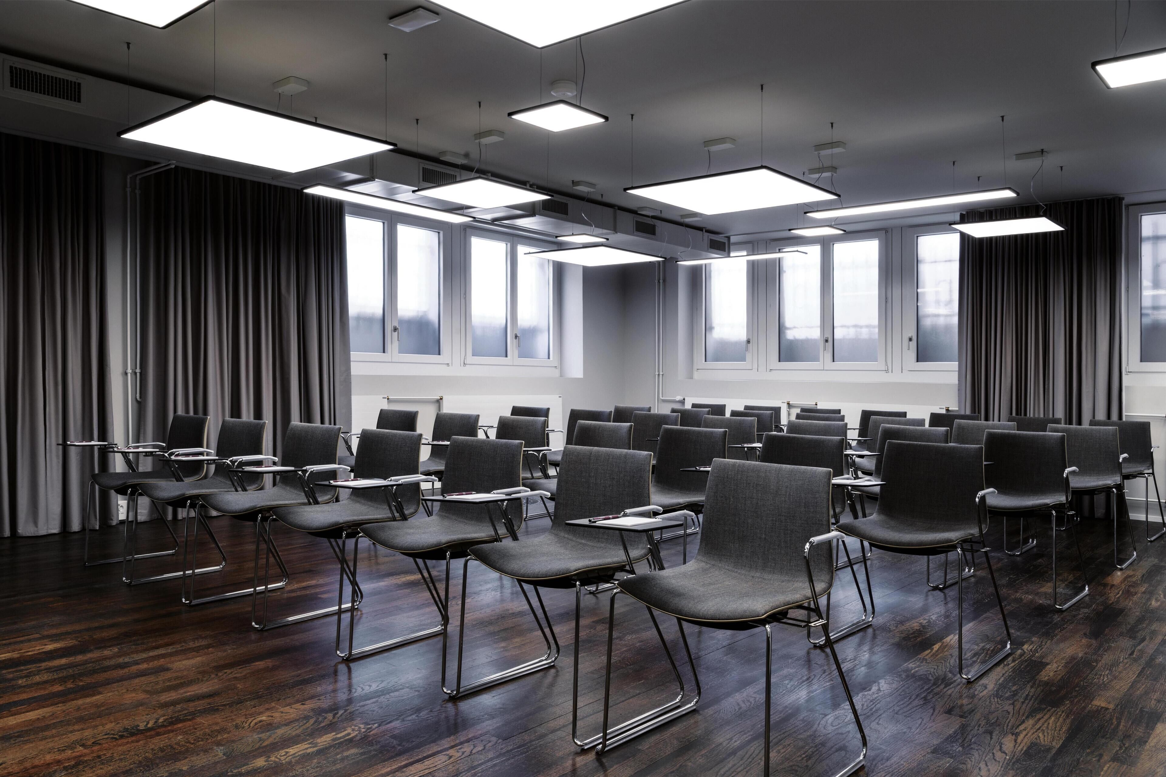 A conference room with rows of chairs, large windows, and ceiling lights.