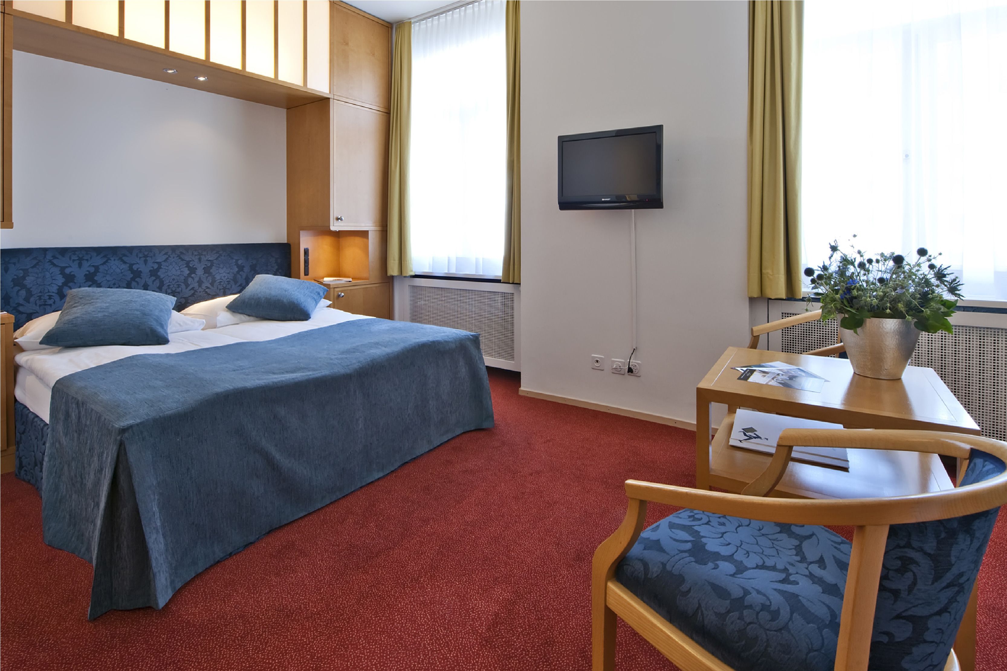 Una habitación de hotel con cama, escritorio, silla, televisor y ventana con cortinas.