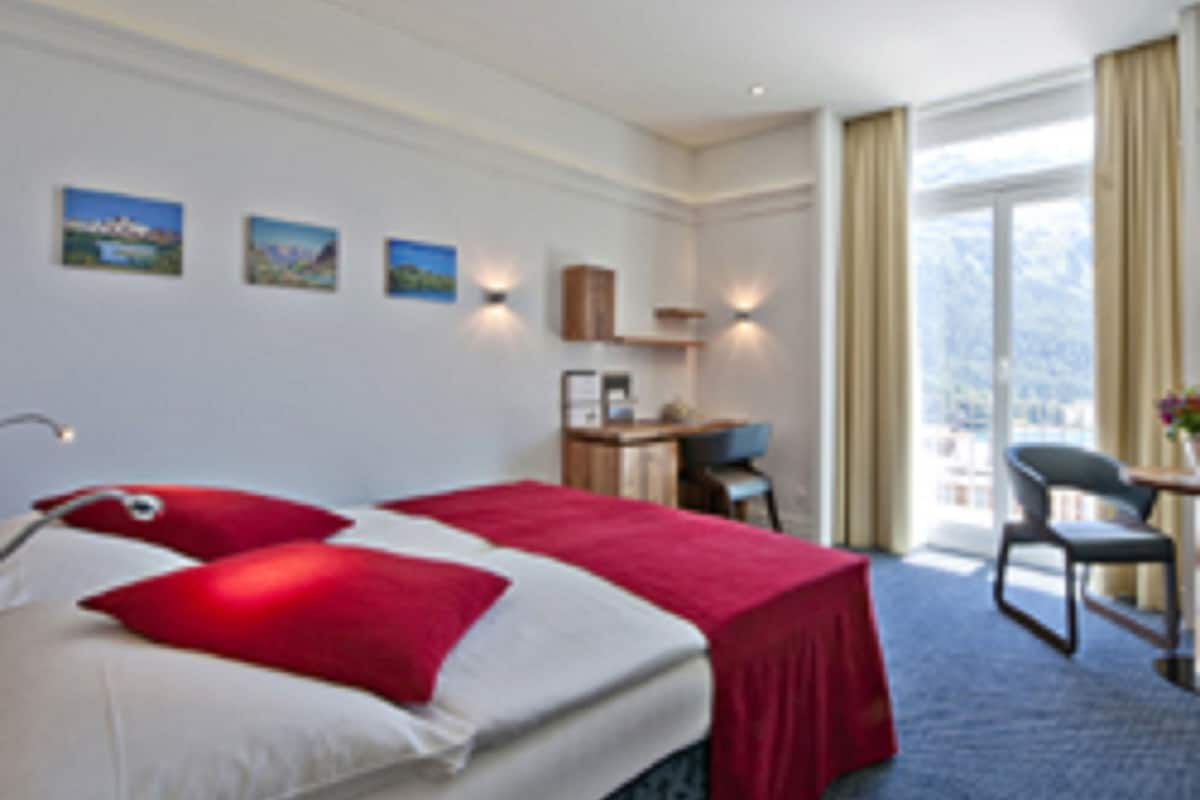 A hotel room with a bed, a desk, and a chair. There are three paintings on the wall.