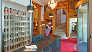 A reception area with a wall-mounted key rack, a reception desk, a potted plant, and a staircase leading to another floor. - Schweizerhof Swiss Quality Hotel (St. Moritz)