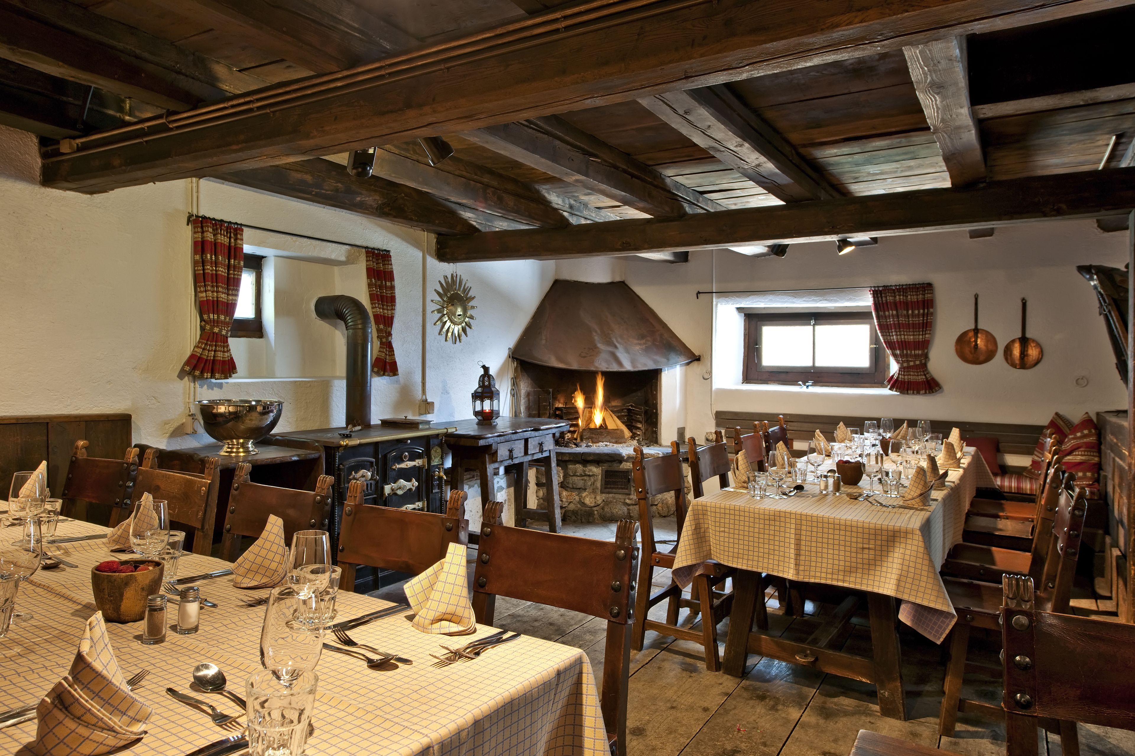 Un comedor rústico con vigas de madera, chimenea de piedra y manteles a cuadros.