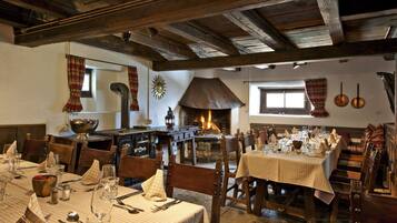 Un comedor rústico con vigas de madera, chimenea de piedra y manteles a cuadros.