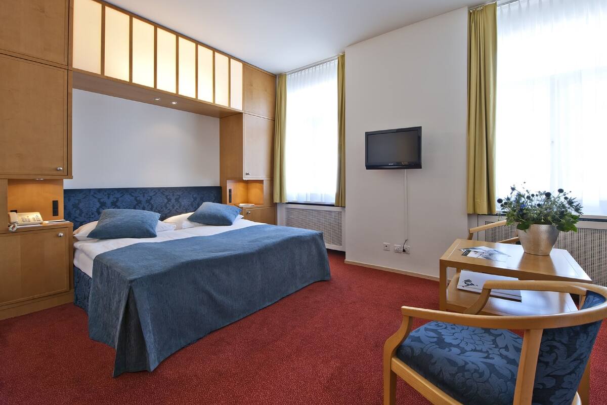 A hotel room with a bed, bedside table, TV, and a desk with a chair.