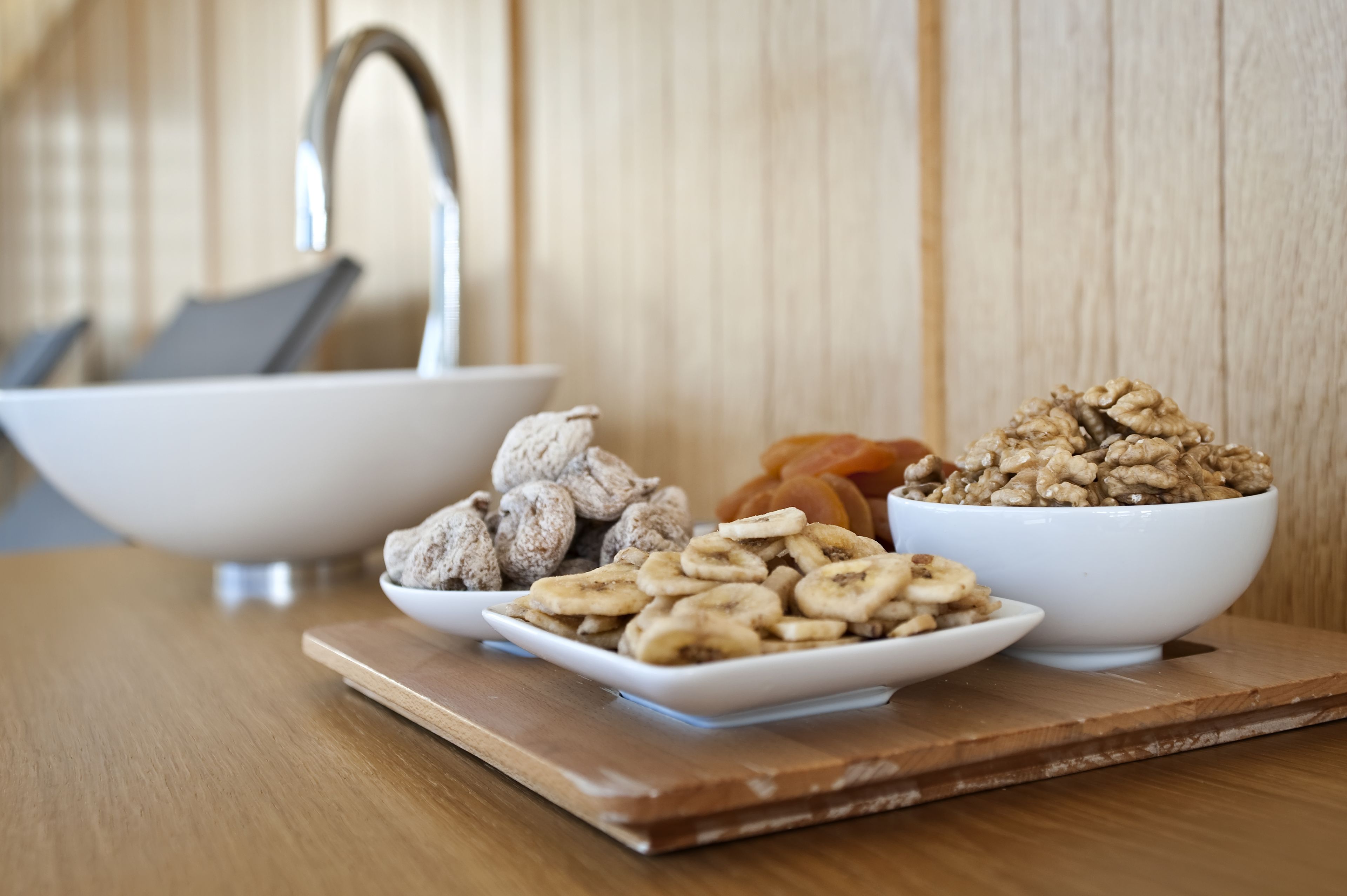 A wooden table with three white bowls containing different snacks.