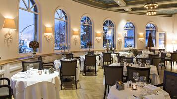 A restaurant with multiple tables set for dining, large arched windows, and chandeliers.