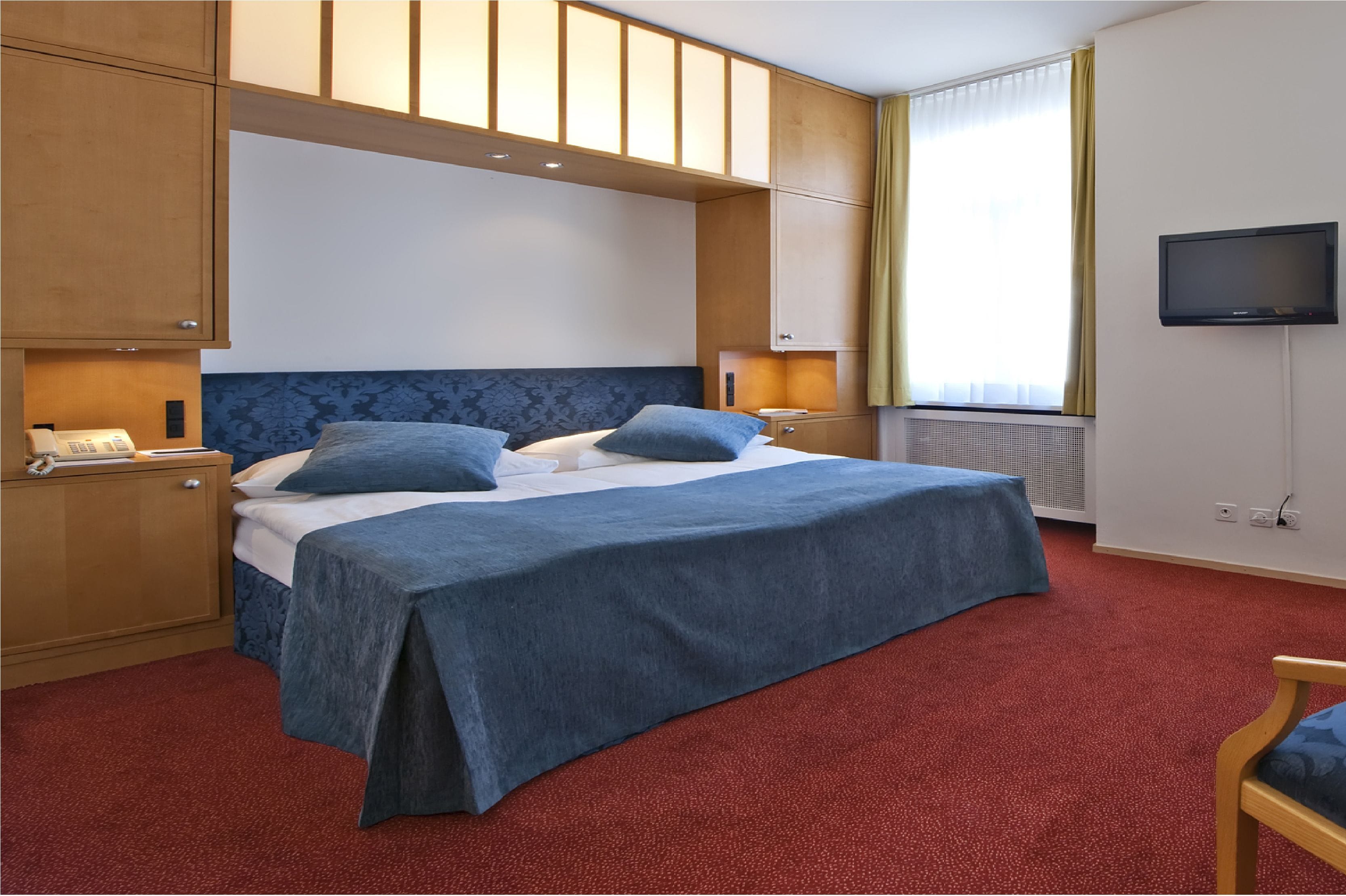 Habitación de hotel con una cama grande, armarios de madera, televisión y alfombra roja.