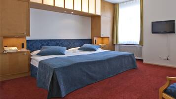 Habitación de hotel con una cama grande, armarios de madera, televisión y alfombra roja.