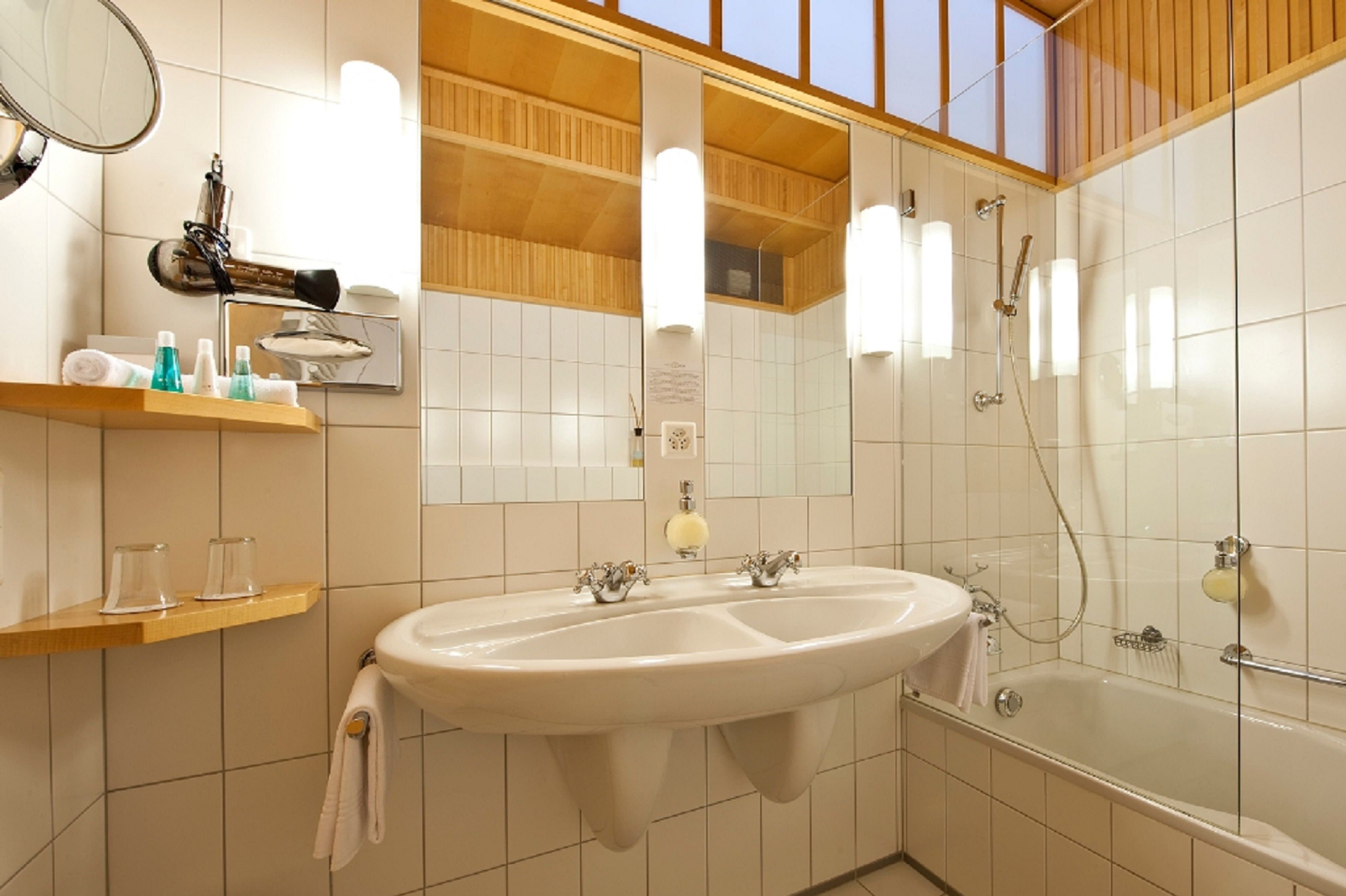 A bathroom with a double sink, a mirror, a hairdryer, and a shower.
