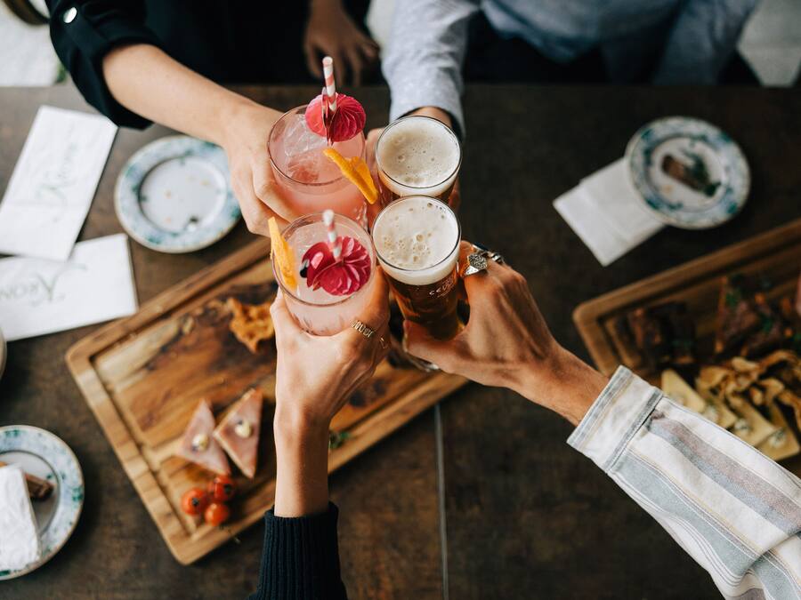 A group of people toasting with drinks at a wooden table with a wooden board of food and plates.