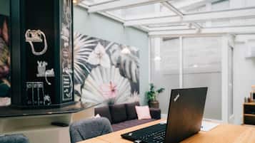 Un espacio de trabajo moderno con un ordenador portátil sobre una mesa de madera, una lámpara de escritorio negra y una gran obra de arte floral en la pared.